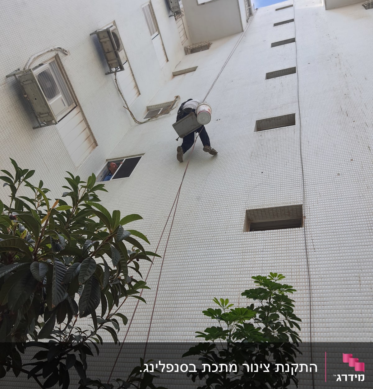 אדם תלוי על חבל עם דלי על קיר בניין